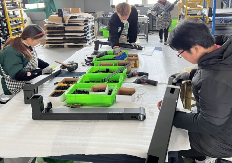 Operators assembling metal frames beside organized component bins at NBFEIYU
